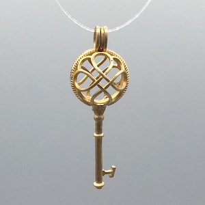 May include: A gold key-shaped pendant with a round, intricate, openwork design. The pendant is on a clear string.