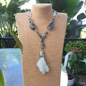 May include: A silver necklace with a white coral pendant and clear and gray gemstone beads. The necklace features silver seahorse charms.