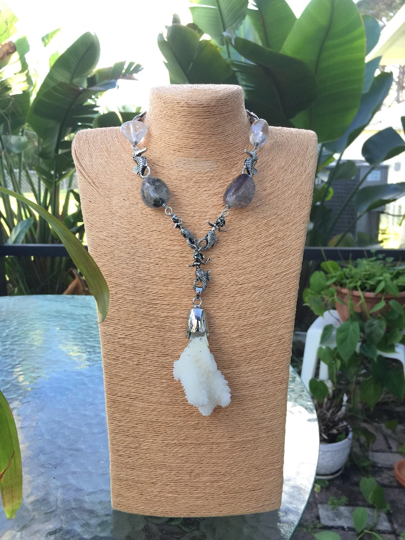 May include: A silver necklace with a white coral pendant and clear and gray gemstone beads. The necklace features silver seahorse charms.
