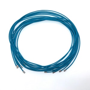 May include: A bundle of teal blue cord, approximately 10 strands, with silver metal tips at the ends.