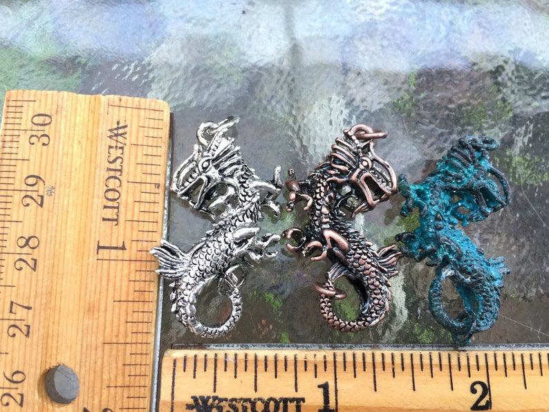 May include: Three silver dragon charms, each with a different finish. The charms are about 1 inch long and are shown next to a ruler for size reference.
