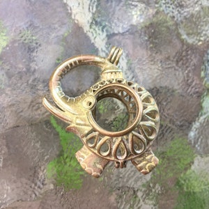 May include: A gold metal elephant figurine with an intricate design. The elephant is standing on its hind legs with its trunk raised. The figurine is made of a hollow metal and has a circular opening in the center.