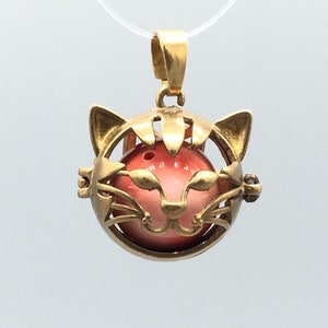 May include: Gold-tone cat-shaped charm with a pink and white orb inside. The charm is a cage-like design with a cat's face on the front.