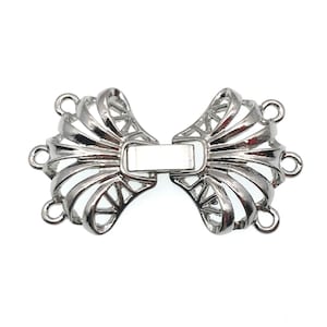 May include: Silver tone metal clasp with a decorative fan-shaped design. The clasp has four loops for attaching to a necklace or bracelet.