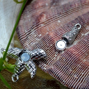May include: Silver tone starfish charm with a magnetic closure. The charm is on a seashell background.