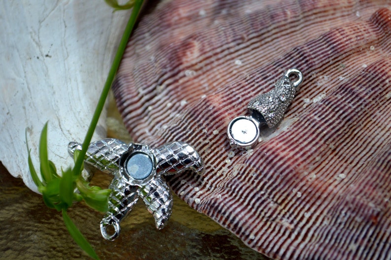 May include: Silver tone starfish charm with a magnetic closure. The charm is on a seashell background.