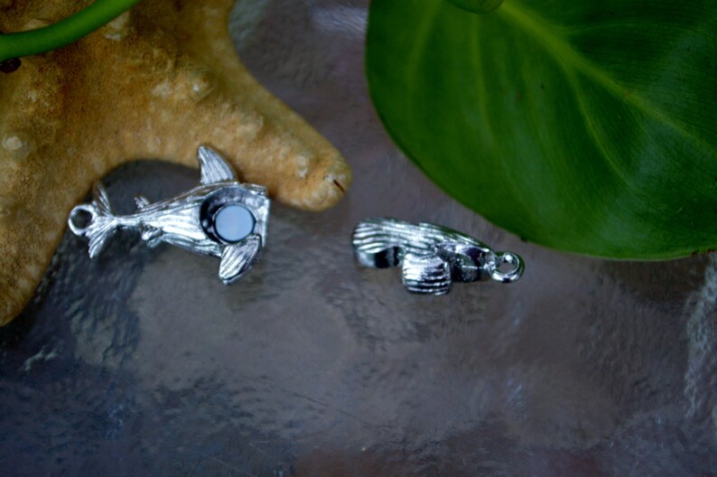May include: Two silver charm pendants, one shaped like a shark and the other like a fish, both with a white stone in the center.