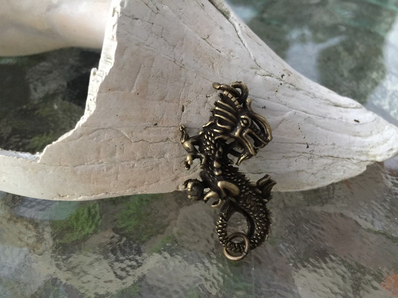 May include: A gold-toned metal dragon charm pendant with intricate details. The dragon is curled up with its tail in its mouth.