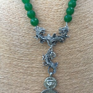 May include: A green jade bead necklace with a silver dragon pendant. The pendant features two dragons facing each other with a third dragon hanging below.