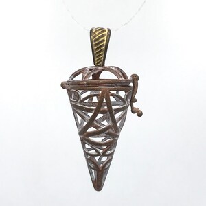 以下が含まれることがあります： 蓋付きの複雑なフィリグリーデザインが施された、銀と金の円錐形のペンダントネックレスです。