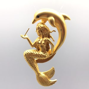Op de afbeelding: Een gouden hanger met een zeemeermin die op een dolfijn rijdt. De zeemeermin houdt een klein voorwerp in haar hand. De hanger is gedetailleerd met textuur schubben en golvend haar.