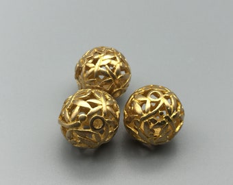 May include: Three gold-colored metal beads with a decorative, openwork design. The beads are round and have a delicate, intricate pattern.