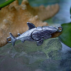 May include: A silver shark charm with a detailed, textured finish. The charm has a loop at the top for attaching to a necklace or bracelet.