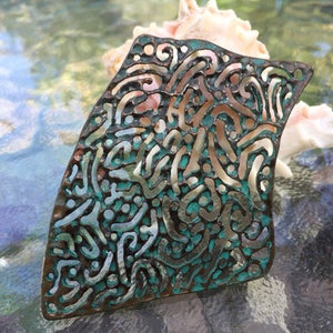 May include: A copper and turquoise patterned metal pendant with a cutout design. The pendant is shaped like a leaf and has a rough, textured surface.