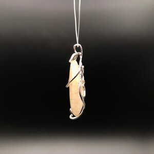 Puede incluir: Un colgante de piedra blanca con un dise&ntilde;o de alambre de plata. El colgante est&aacute; colgado de una cadena de plata.