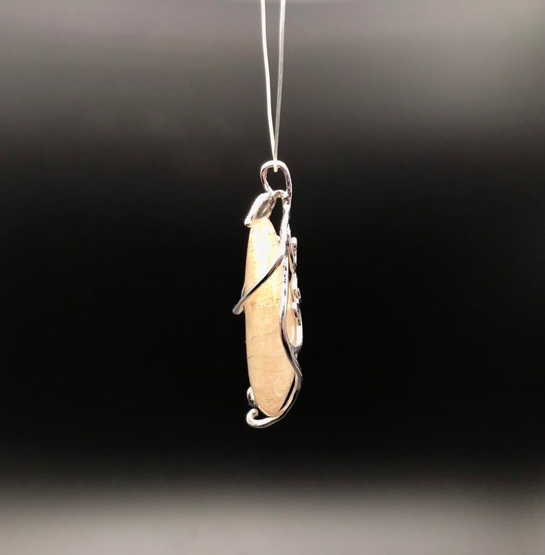 Puede incluir: Un colgante de piedra blanca con un dise&ntilde;o de alambre de plata. El colgante est&aacute; colgado de una cadena de plata.