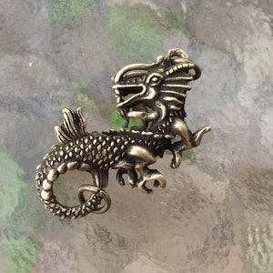 May include: A gold-toned metal dragon pendant with intricate details. The dragon is curled up with its tail in its mouth.