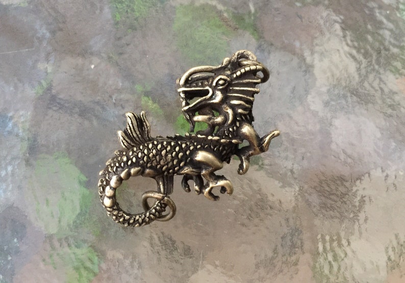 May include: A gold-toned metal dragon pendant with intricate details. The dragon is curled up with its tail in its mouth.