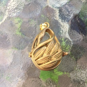 May include: A gold-toned metal birdcage pendant with a detailed design of leaves and a bird inside. The cage is open on one side and has a small loop at the top for attaching a chain.