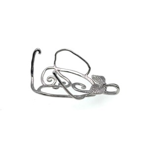 Puede incluir: Pendiente de metal plateado con un dise&ntilde;o delicado y ornamentado con un motivo de hoja. El pendiente tiene un bucle en la parte superior para sujetarlo a una cadena o cord&oacute;n.