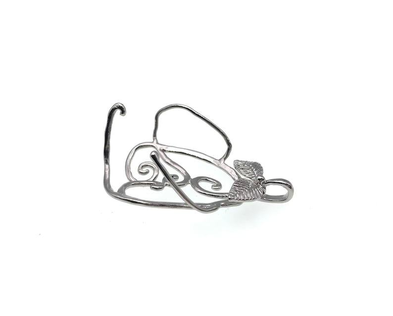 Puede incluir: Pendiente de metal plateado con un dise&ntilde;o delicado y ornamentado con un motivo de hoja. El pendiente tiene un bucle en la parte superior para sujetarlo a una cadena o cord&oacute;n.