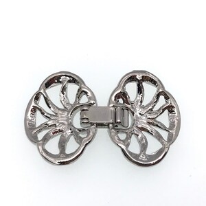 Puede incluir: Cierre de metal plateado con un dise&ntilde;o decorativo calado. El cierre tiene forma de dos c&iacute;rculos superpuestos con un patr&oacute;n floral detallado.