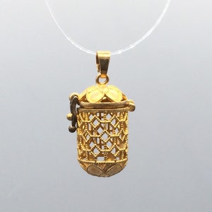 May include: A gold-toned filigree pendant with a hinged lid. The pendant is shaped like a small cylinder and has a delicate, intricate design.