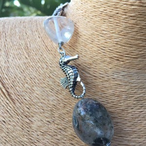 May include: A silver necklace with a clear crystal bead, a silver seahorse charm, and a grey agate bead.
