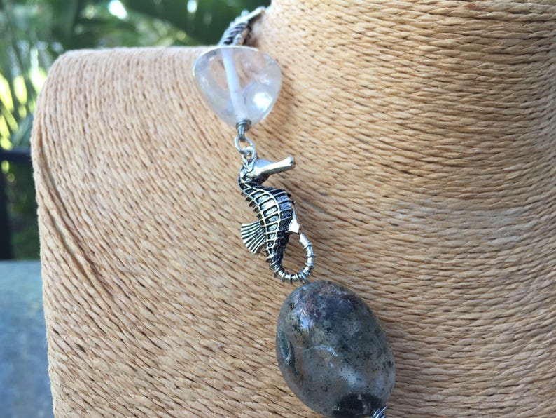 May include: A silver necklace with a clear crystal bead, a silver seahorse charm, and a grey agate bead.