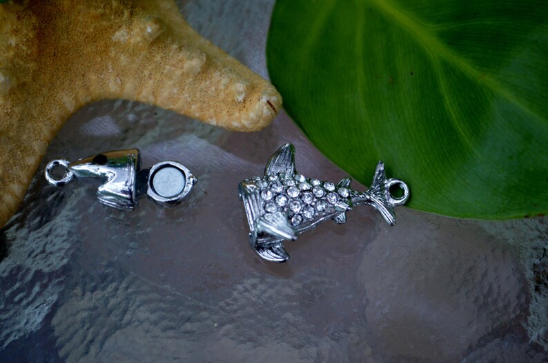 May include: A silver charm in the shape of a shark with rhinestones. The charm is open and has a magnetic closure.
