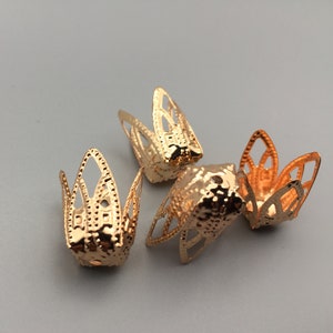 Puede incluir: Cuatro tapones decorativos de metal de color dorado con un diseño floral. Los tapones tienen una superficie texturizada y están diseñados para ser utilizados en cordones u otros materiales.