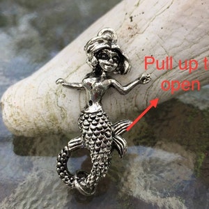 May include: Silver mermaid charm with a detailed design. The tail of the mermaid is hinged and can be pulled up to open.