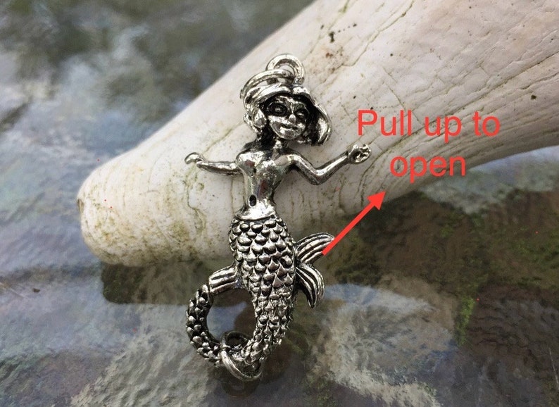 May include: Silver mermaid charm with a detailed design. The tail of the mermaid is hinged and can be pulled up to open.