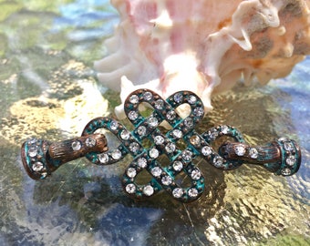 May include: A turquoise and copper-toned metal clasp with a knot design, embellished with clear rhinestones.