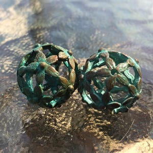 May include: Two teal-colored metal spheres with a decorative, floral design. The spheres are made of a wire mesh with a floral pattern.