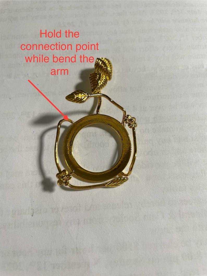 Puede incluir: Porta anillos de metal dorado con un dise&ntilde;o floral decorativo. El porta anillos tiene una base circular y un tallo delicado con hojas y flores.
