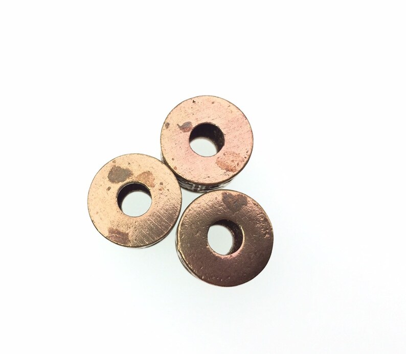 Puede incluir: Tres cuentas redondas de metal de color cobre con un agujero en el centro. Las cuentas est&aacute;n dispuestas en forma de tri&aacute;ngulo.
