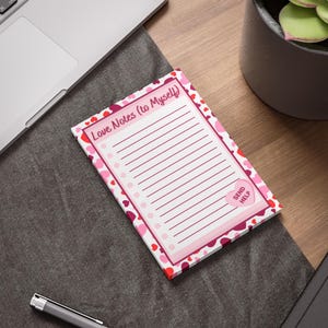 Pode incluir: Um bloco de notas retangular com o texto "Love Notes (to Myself)" e páginas pautadas. O bloco de notas tem uma borda rosa com desenhos em forma de coração em tons de vermelho e rosa. Um coração rosa com as palavras "Send Help" está no canto inferior direito.
