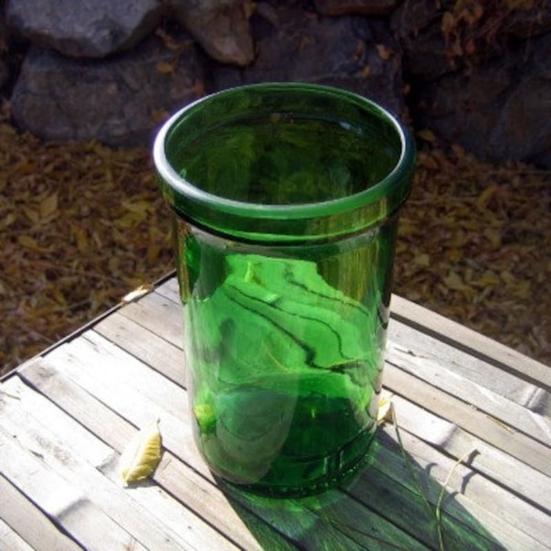 May include: A dark green glass vase with a rounded top and a smooth, shiny surface. The vase is sitting on a wooden surface.