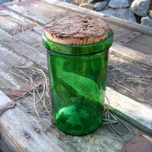 May include: A green glass bottle with a cork lid. The bottle is sitting on a wooden surface.