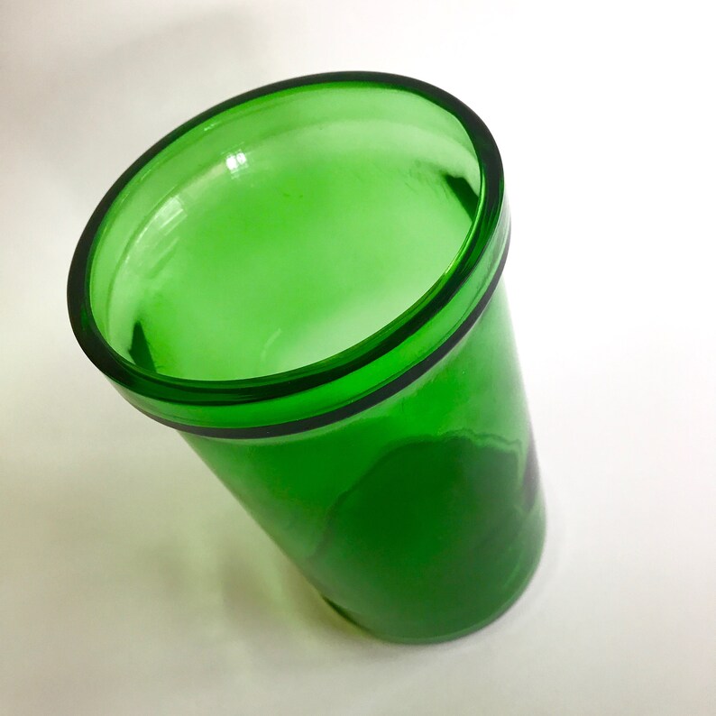 May include: A green glass cup with a wide rim. The cup is empty and appears to be made of thick glass.