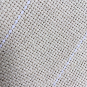 Op de afbeelding: Close-up van een beige stof met witte strepen. De stof heeft een geweven textuur.