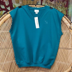 May include: Teal sleeveless v-neck sweater with a small logo on the front. The sweater is sitting on a wicker chair.