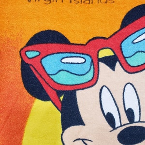 May include: A yellow beach towel featuring Mickey Mouse wearing sunglasses in red, white and blue. The towel has the text "St. Thomas Virgin Islands" printed on it.