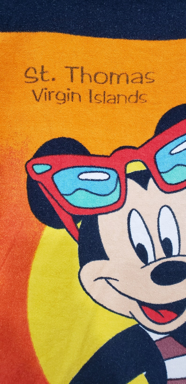 May include: A yellow beach towel featuring Mickey Mouse wearing sunglasses in red, white and blue. The towel has the text "St. Thomas Virgin Islands" printed on it.