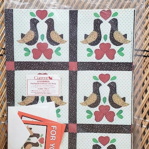 Puede incluir: Un paquete de papel de regalo de estilo patchwork con un patr&oacute;n de p&aacute;jaros negros y marrones con corazones rojos y hojas verdes sobre un fondo blanco con lunares negros. El paquete incluye dos etiquetas de regalo que dicen "Para Ti". El paquete est&aacute; etiquetado "Current's Lovebirds Patchwork Patterns Gift Wrap 2-7/8' x 11' Rolls 2 Gift Cards & Envelopes CODE 1785"