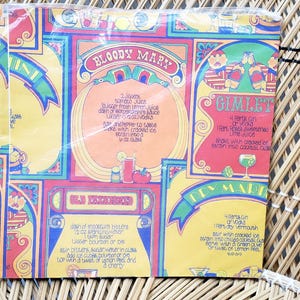 Puede incluir: Un papel de envolver vintage colorido para recetas de c&oacute;cteles con un dise&ntilde;o amarillo, rojo y azul. El papel presenta recetas de c&oacute;cteles Bloody Mary, Gimlet, Old Fashioned y Tom Collins.