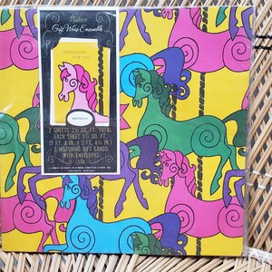 Puede incluir: Un conjunto de papel de regalo vintage con un dise&ntilde;o de carrusel con caballos coloridos y remolinos sobre un fondo amarillo. El texto en el paquete dice "The Majestic Gift Wrap Ensemble 1 sheet 23.5" x 30.5" total each sheet is 23.5" x 15.25" 2 gift bags 8" x 10" with matching gift cards with envelopes 5.5" x 4.25".