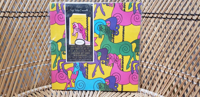 Puede incluir: Un conjunto de papel de regalo vintage con un dise&ntilde;o de carrusel con caballos coloridos y remolinos sobre un fondo amarillo. El texto en el paquete dice "The Majestic Gift Wrap Ensemble 1 sheet 23.5" x 30.5" total each sheet is 23.5" x 15.25" 2 gift bags 8" x 10" with matching gift cards with envelopes 5.5" x 4.25".