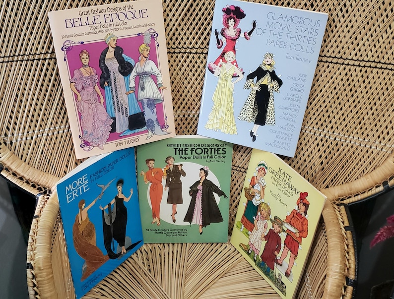 Puede incluir: Una colecci&oacute;n de libros de mu&ntilde;ecas de papel vintage con dise&ntilde;os de moda de la Belle &Eacute;poque, la d&eacute;cada de 1930 y la de 1940. Los libros muestran ilustraciones coloridas de trajes hist&oacute;ricos y atuendos de estrellas de cine. Los t&iacute;tulos incluyen "Great Fashion Designs" y "Glamorous Movie Stars".